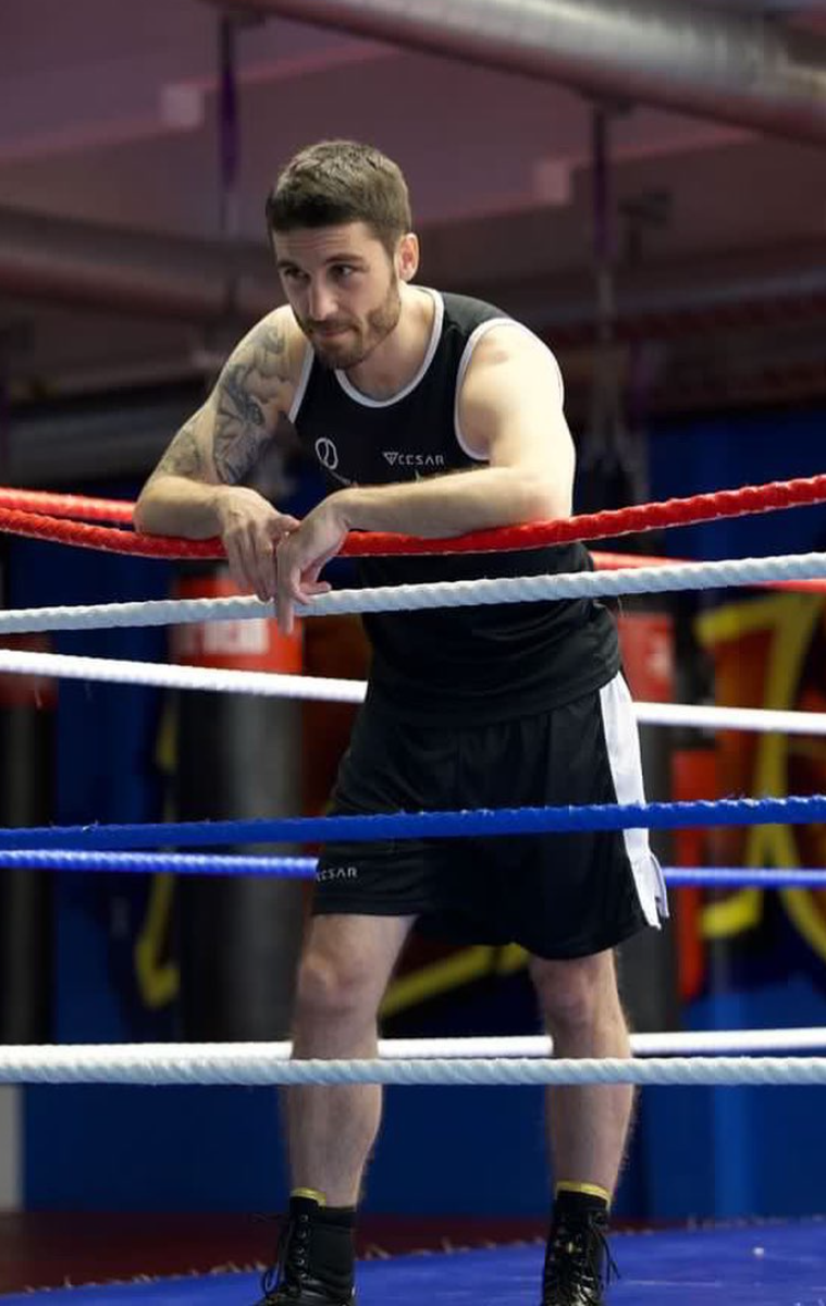 Professional boxer José Antonio Sánchez Rayito resting his arms forward on the red ropes inside a boxing ring
